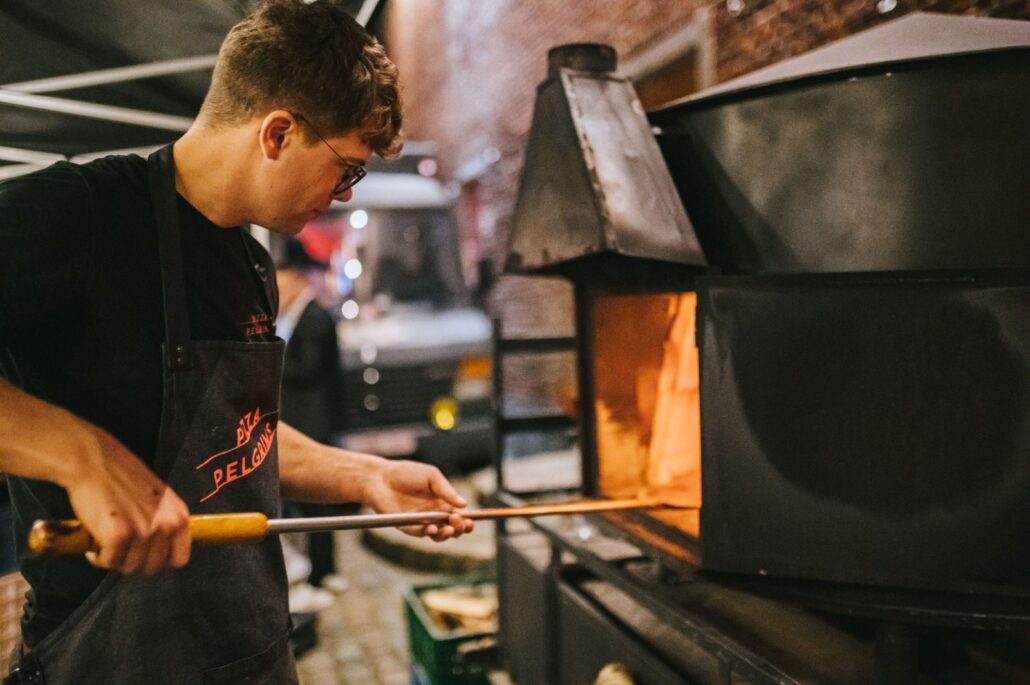 Pizzabakker schuift een pizza in de houtoven van de foodtruck