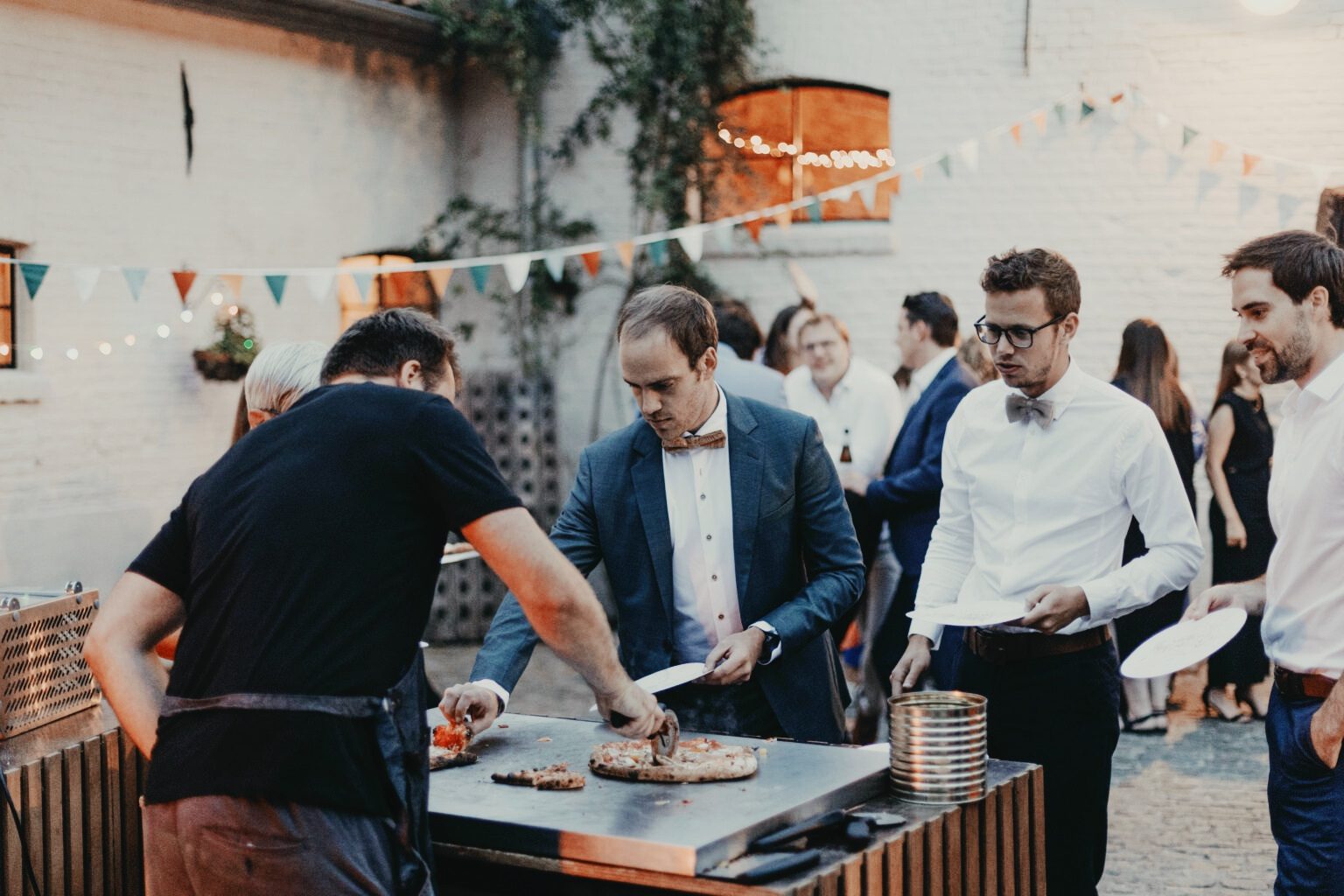 Gasten in feestkledij halen pizza aan de stand van Pizza Pelgrims op een binnenkoer
